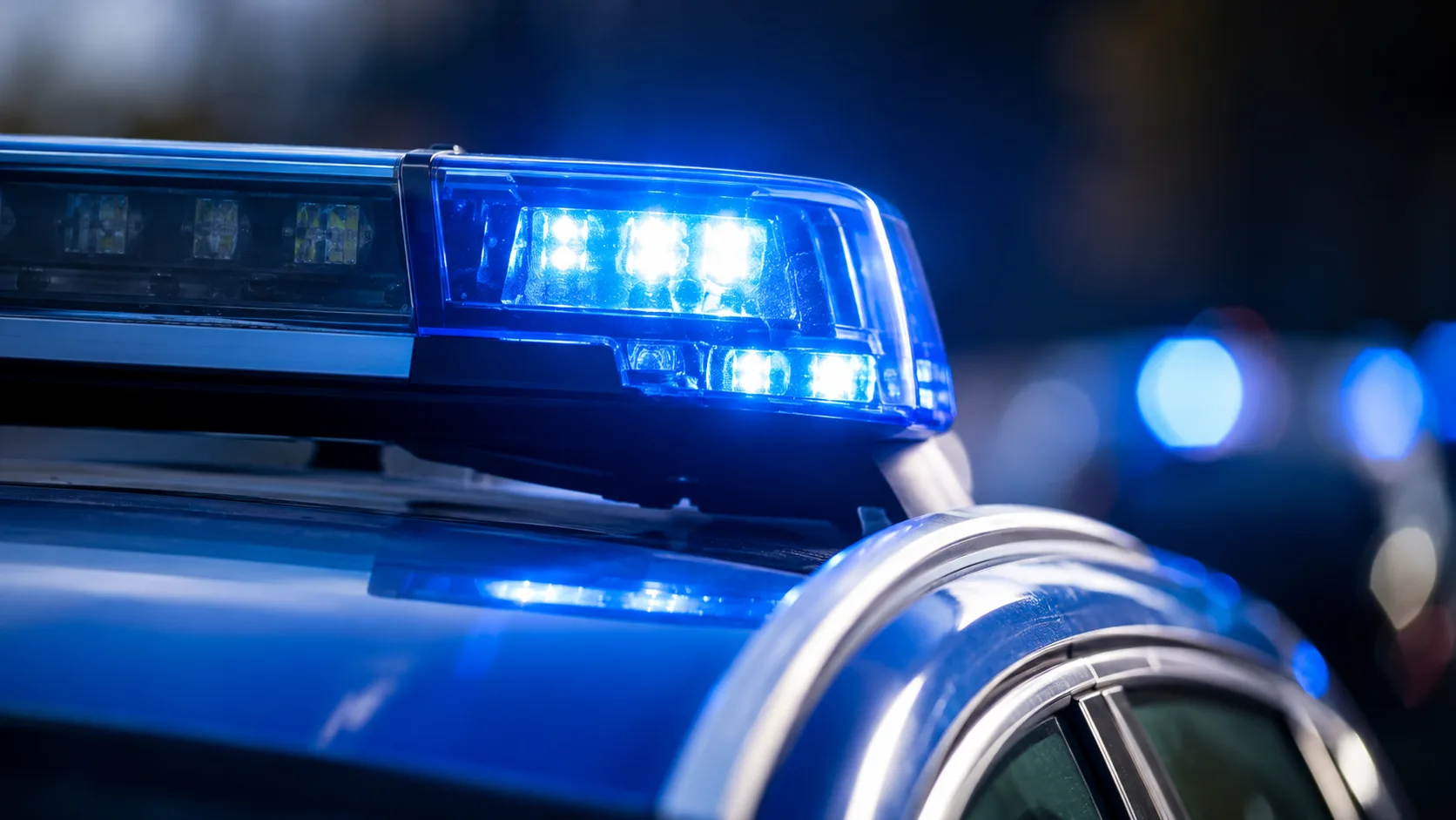 Blau leuchtendes Warnlicht auf dem Dach eines neutralen Polizeifahrzeugs vor dunklem Hintergrund.