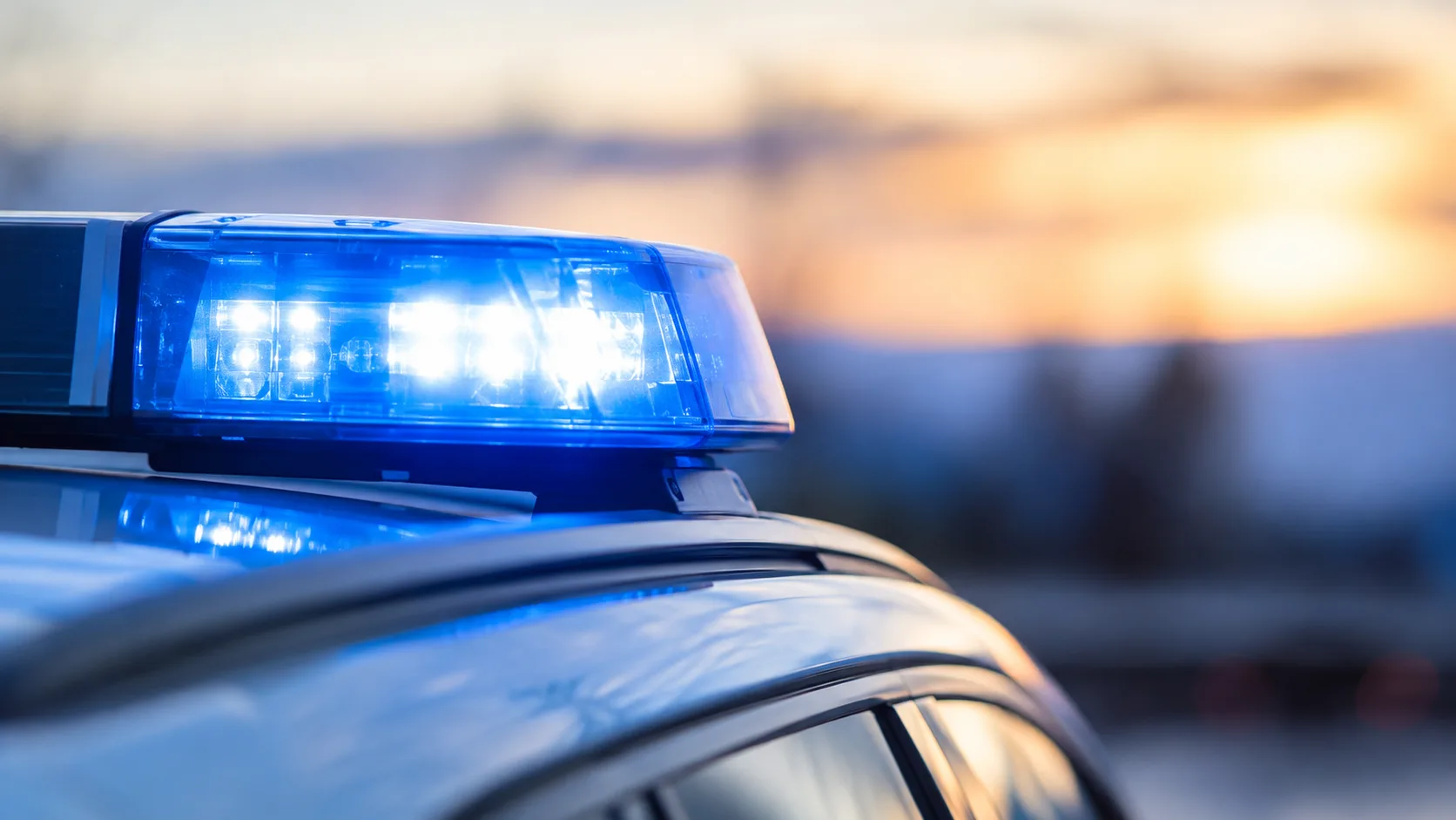 Blaulicht auf dem Dach eines neutralen Polizeifahrzeugs vor unscharfem Hintergrund ohne erkennbare Ortsmerkmale.