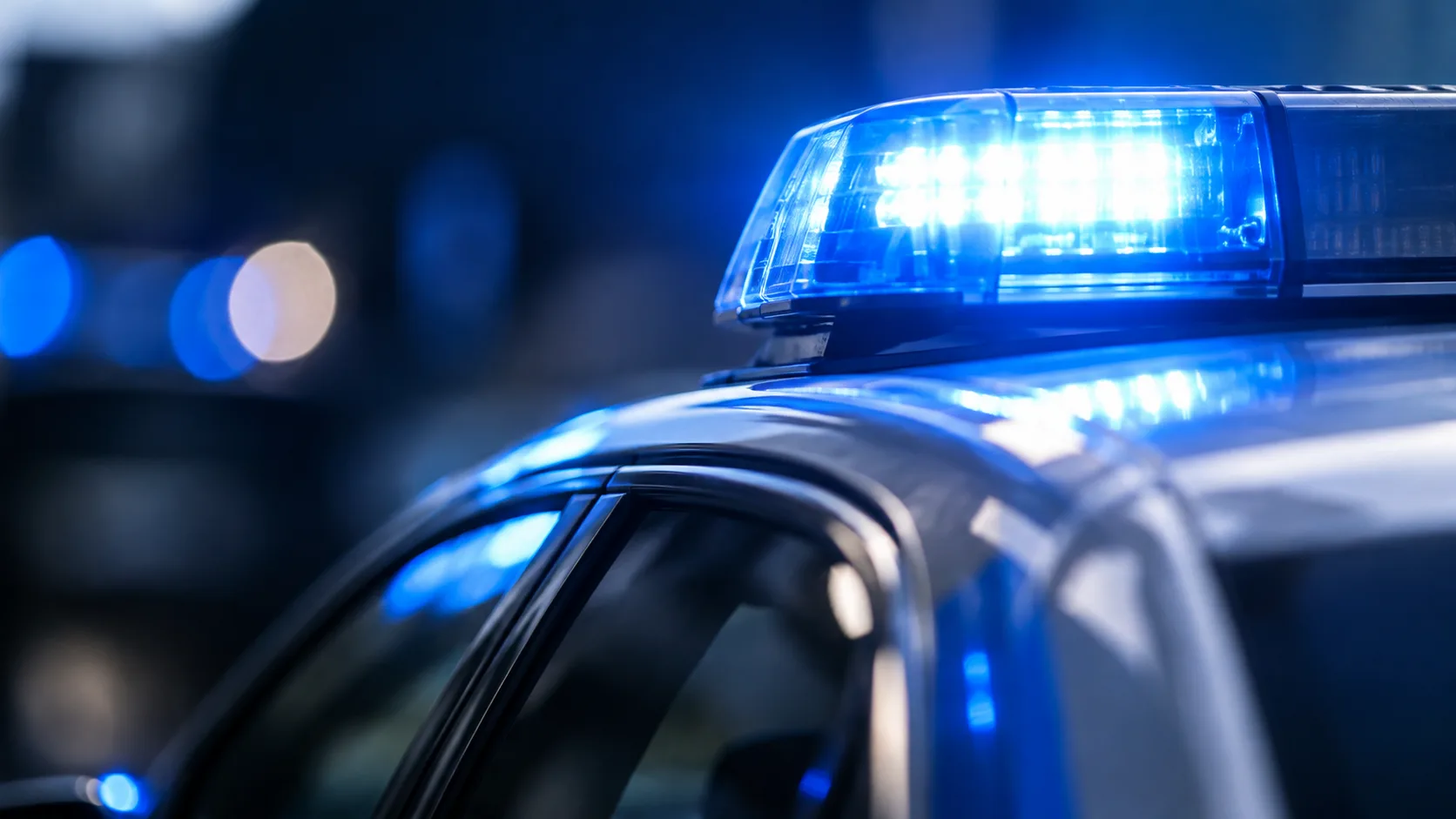 Blaulicht auf dem Dach eines neutralen Polizeifahrzeugs vor dunklem Hintergrund.