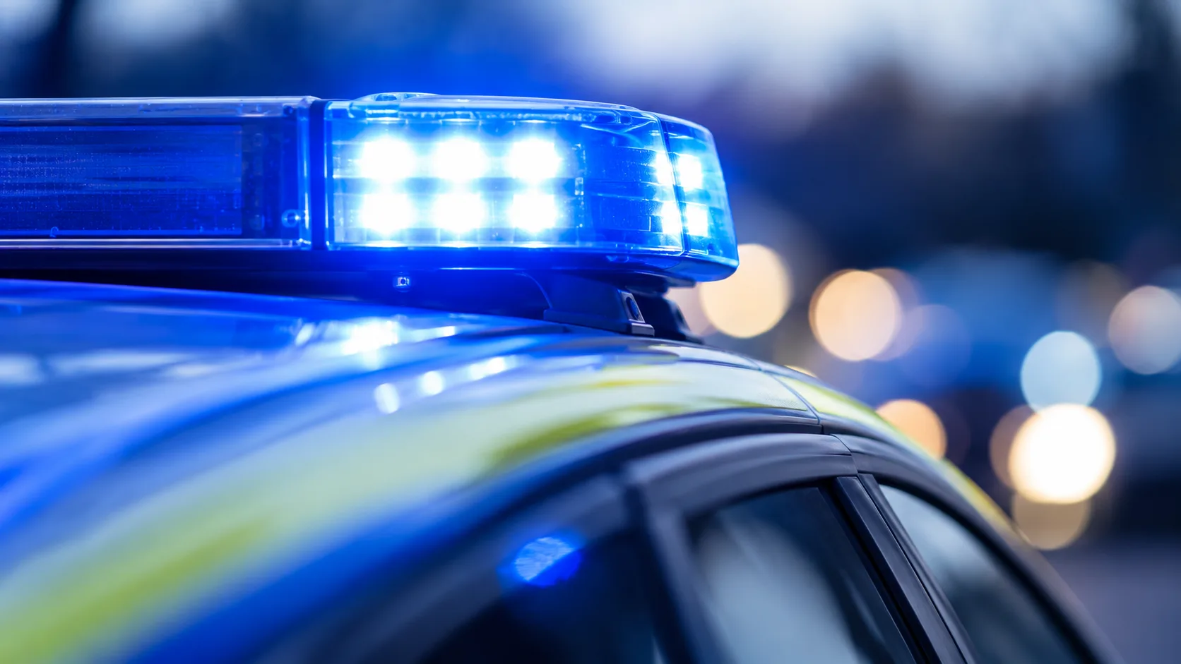 Blau leuchtendes Warnlicht auf einem Polizeifahrzeug vor dunklem, unscharfem Hintergrund.