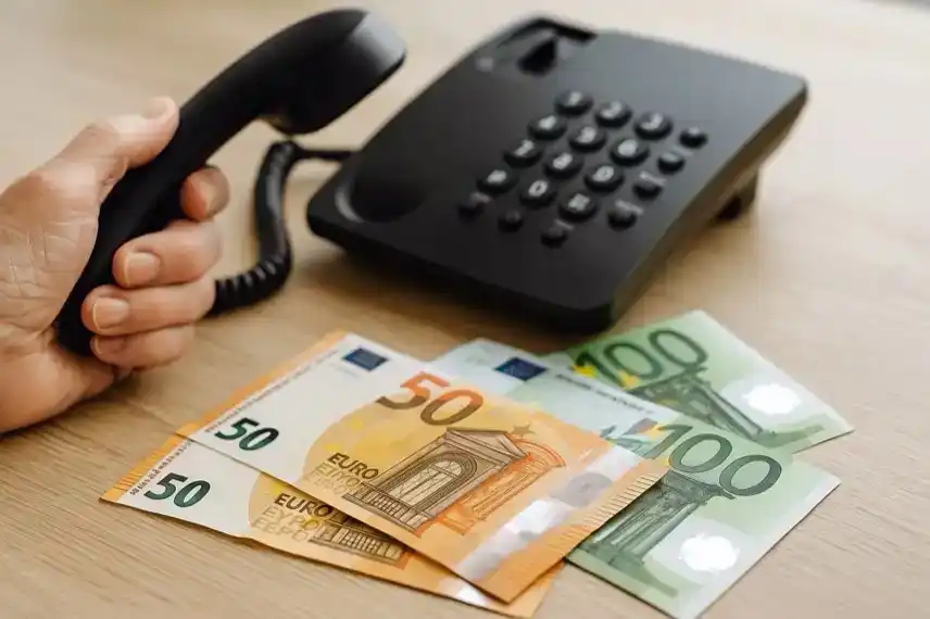 Schockanruf in Weißenfels: Hand mit Telefonhörer neben 50- und 100-Euro-Scheinen auf Holztisch.
