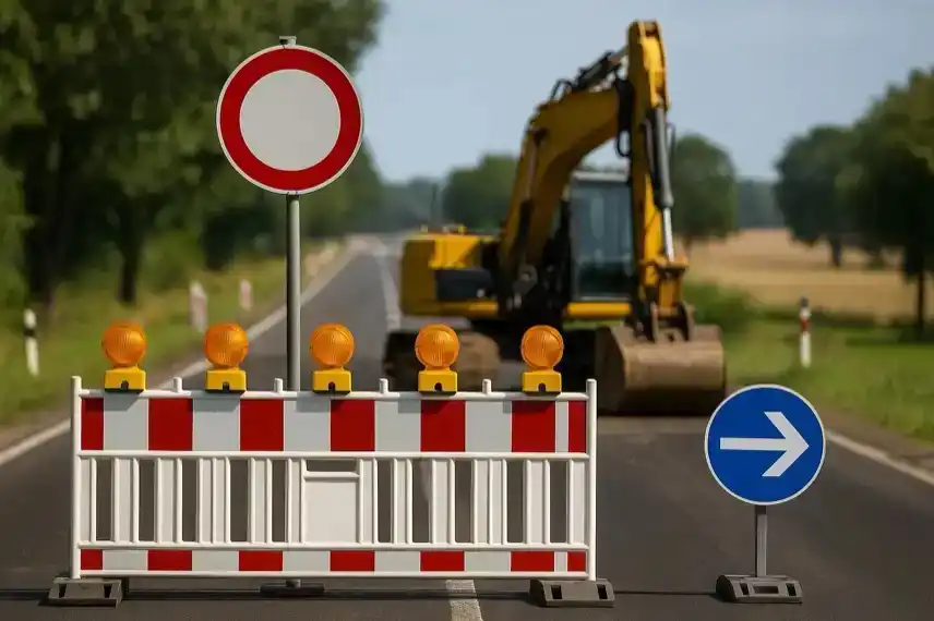 Straßensperre mit Absperrbake, Verkehrszeichen und Bagger auf einer Landstraße bei sonnigem Wetter.