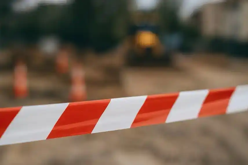 Nahaufnahme eines rot-weißen Absperrbandes vor unscharfem Baustellenhintergrund bei Tageslicht.