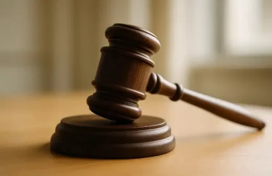 Ein hölzerner Richterhammer liegt auf einer Holzunterlage in einem hellen Raum.