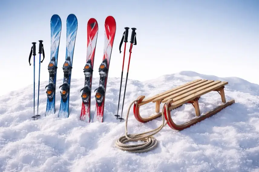 Symbolbild: Mehrere Skifahrer und ein Schlitten bewegen sich auf einer schneebedeckten Anhöhe. Die Szene steht stellvertretend für Wintersportaktivitäten bei guten Schneeverhältnissen.