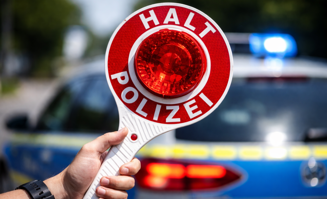 Hand hält Polizeikelle bei Verkehrskontrolle vor Polizeiauto, Kontrolle im Straßenverkehr wegen Alkoholfahrt